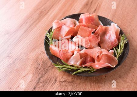 Charcuterie-Platte mit Proscuitto serviert mit Oliven auf Holztisch Hintergrund mit Kopieplatz. Schwarzer Teller mit traditionellen italienischen Antipasti. Auswahl Stockfoto