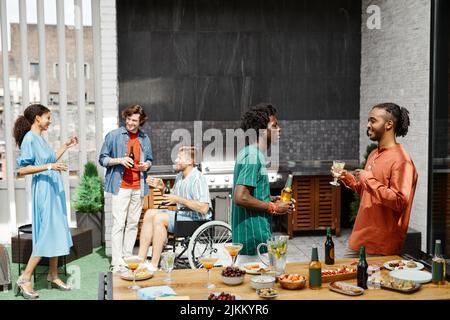 Diverse Gruppe von Freunden genießen Party auf der Terrasse und Kommunikation, einschließlich Person im Rollstuhl Stockfoto