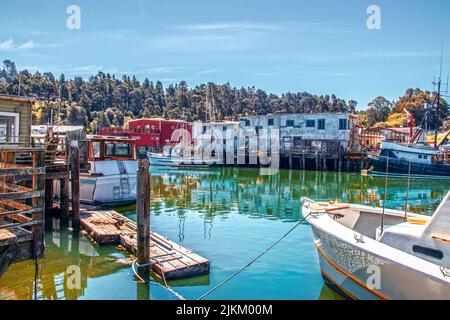 Fischerboote vertäuten an einem alten, funktionierenden Hafen und Docks mit heruntergezogenem Gebäude, die sich in türkisem Wasser in Ft. Bragg CA USA Stockfoto