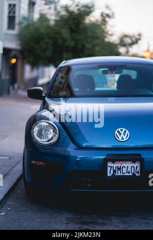 Eine vertikale Aufnahme eines blauen Volkswagen-Käfer, der an einem Bürgersteig geparkt ist Stockfoto