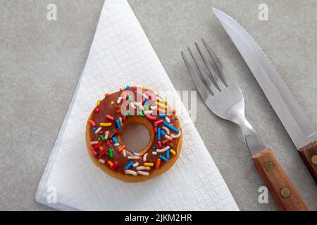 Eine Draufsicht auf eine Schokolade streuen Donut auf ein Gewebe und Besteck Stockfoto