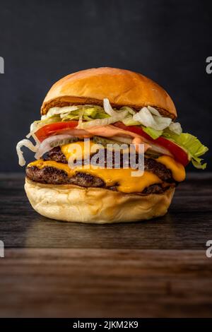 Eine vertikale Aufnahme eines leckeren saftigen Burgers mit Gemüse auf einem Holztisch Stockfoto