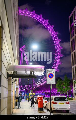 LONDON - 17. Mai 2022: London Eye leuchtet bei Nacht in lila neben den County Hall Apartments Stockfoto