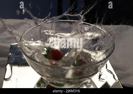 Eine Nahaufnahme einer Erdbeere, die in eine mit Wasser gefüllte Schüssel fällt. Stockfoto