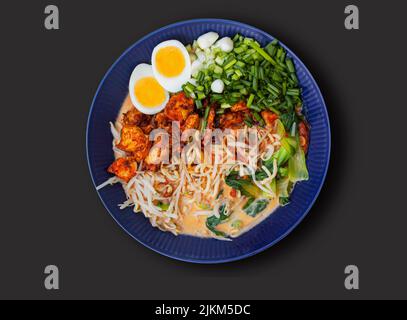 Japanische Ramen-Suppe mit Nudeln, Huhn, Ei, Schnittlauch, Frühlingszwiebeln, bok Choy und Sprossen. Draufsicht von oben auf schwarzem Hintergrund. Stockfoto
