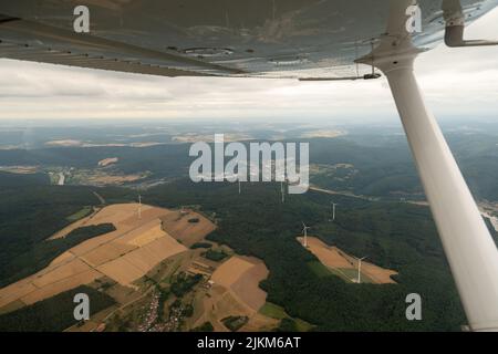 Collenberg, Bayern, Deutschland, 10. Juli 2022 Windenergieanlagen rotieren auf einem grünen Hügel, von einem kleinen Flugzeug aus gesehen Stockfoto