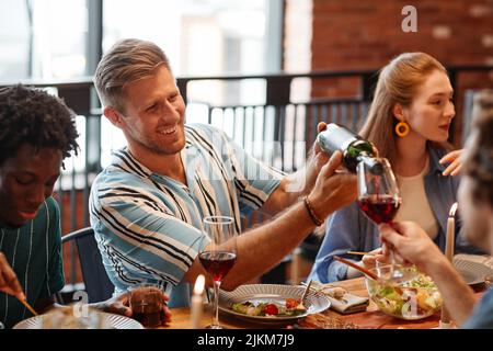 Porträt eines lächelnden Mannes, der Wein ins Glas gießt, während er mit Freunden in gemütlicher Atmosphäre eine Dinnerparty genießt Stockfoto