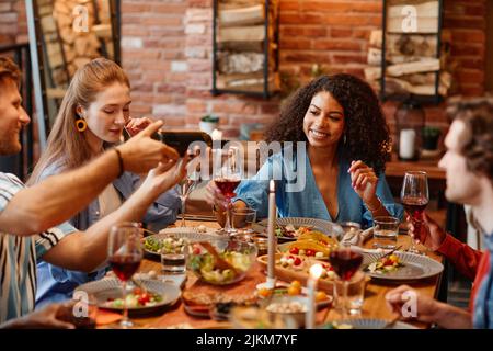 Porträt einer schwarzen jungen Frau, die während der Dinner-Party mit Freunden in gemütlicher, warmer Umgebung ein Glas Wein genießt Stockfoto