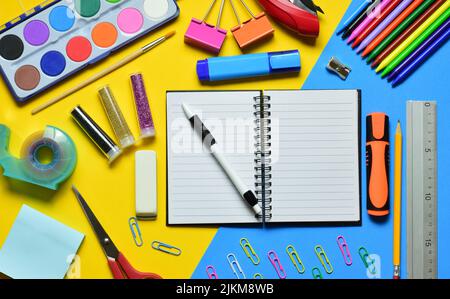 Ein offenes Notizbuch mit einem Stift und einem Briefpapier auf gelb-blauem Hintergrund Stockfoto