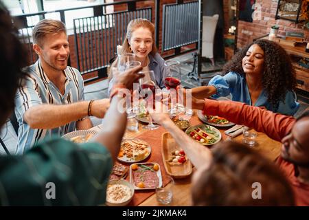 Eine vielfältige Gruppe junger Menschen, die mit Weingläsern toasten, während sie zusammen eine Dinner-Party feiern, Copy Space Stockfoto