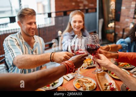 Nahaufnahme von jungen Leuten, die mit Weingläsern rösten, während sie zusammen eine Dinner-Party feiern, Kopierraum Stockfoto
