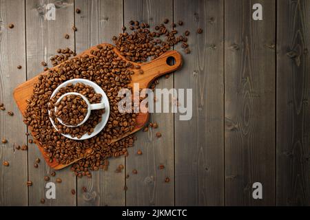 Eine Draufsicht auf Kaffeebohnen auf einem Holzbrett und in der Kaffeetasse auf einem Holzhintergrund Stockfoto