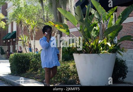 Eine afroamerikanische Frau, die einen Bürgersteig entlang geht, während sie im St. Johns Town Center telefoniert Stockfoto