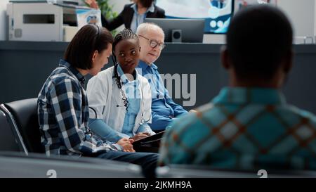 Hausärztin, die asiatische Patienten in der Lobby des Wartebereichs konsultiert, um eine Krankheitsdiagnose und eine Gesundheitsbehandlung zu geben. Arzt, der kranke Menschen an der Krankenhausaufnahme unterstützt. Stockfoto