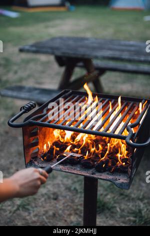 Eine vertikale Aufnahme einer brennenden Flamme in einem Grillofen im Freien neben einem Picknicktisch. Stockfoto