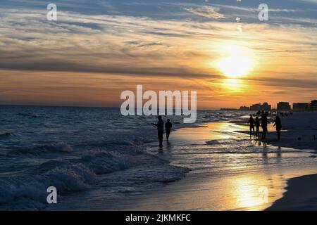 Eine Silhouette von Menschen, die während des Sonnenuntergangs am Strand in Destin, Florida, USA, spazieren gehen Stockfoto