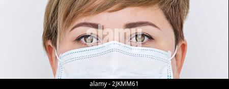 Junge kaukasische Frau trägt blaue chirurgische Gesichtsmaske Nahaufnahme Breitbild-Porträt Stockfoto