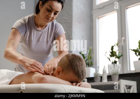 Masseur gibt dem Kind eine Rückenmassage. Kinder Massage-Konzept. Massage-Therapeut gibt 7 Jahre alten Jungen Schulter-Massage. Physiotherapie Stockfoto