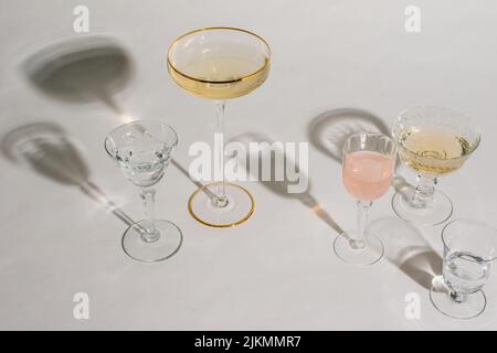 Anordnung verschiedener Cocktailgläser auf weißem Hintergrund mit rosa und goldener Flüssigkeit Stockfoto