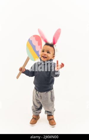 Lächelnd aufgeregt afro amerikanischen fünf Jahre alten Jungen Spaß mit osterhasen Ohren hält ein großes Spielzeug osterei auf dem Stock - isoliert. Hochwertige Fotos Stockfoto