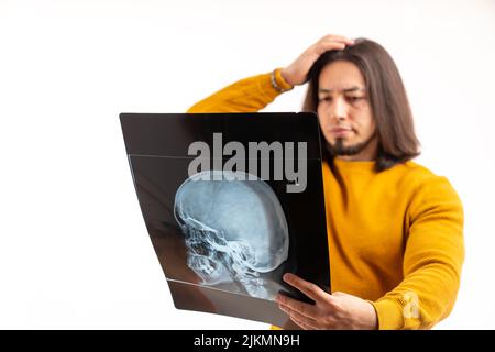 Kaukasischer Mann in seinem 30s trägt gelben Pullover und Analyse Röntgenaufnahme seines Schädels transparentes Bild. Hochwertige Fotos Stockfoto