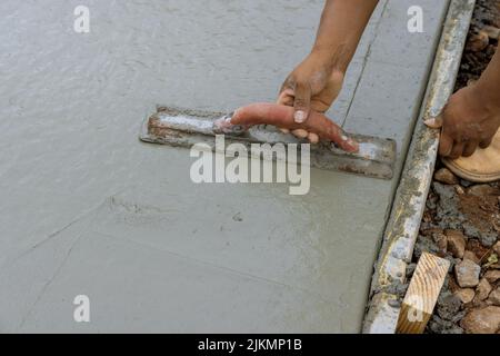 Ein Arbeiter arbeitet an einem neuen Bürgersteig, der gerade auf nassen Beton gegossen wurde, während er eine Stahlkelle hält Stockfoto