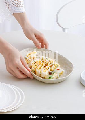 Eine Nahaufnahme von erwachsenen weiblichen Händen, die einen Teller Dan Bing (taiwanesisches Eiercrepe) auf einen weißen Tisch legen Stockfoto