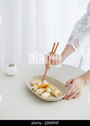 Eine Nahaufnahme von erwachsenen weiblichen Händen, die ein Stück Dan Bing (taiwanesisches Ei) mit Holzstäbchen nahmen Stockfoto