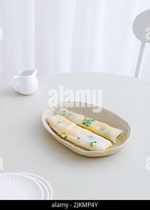 Nahaufnahme von zwei Dan Bing Rollen (taiwanesisches Eiercrepe) in weißem Porzellanteller auf einem weißen Tisch Stockfoto