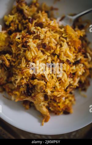 Zereshk Polo BA morgh, Servieren von persischem Safran-Basmati-Reisgericht mit Heidelbeeren und Huhn in einer weißen Schüssel mit Gabel Stockfoto