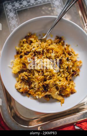 Zereshk Polo BA morgh, Servieren von persischem Safran-Basmati-Reisgericht mit Heidelbeeren und Huhn in einer weißen Schüssel mit Gabel Stockfoto