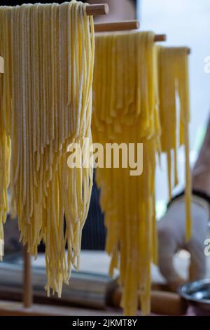 Ein Porträt von frisch zubereiteter Pasta, die auf einem Nudeltrockner hängt Stockfoto