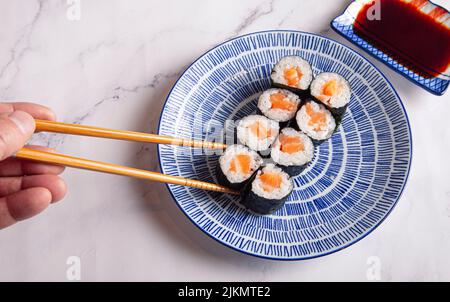 Maki rollt mit Lachs. Die Hand des Mannes hält eine Rolle mit Essstäbchen. Stockfoto