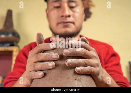 Ein lateinischer Töpfer, der in seiner Werkstatt mit beiden Händen ein Keramikgefäß anstellt und formt. Stockfoto