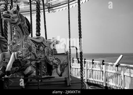 Eine Graustufenaufnahme einer leeren Merry-Go-Round-Fahrt auf dem Brighton Pier am Meer mit grauem Himmel, Großbritannien Stockfoto