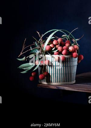 Vorderansicht von frischen reifen Litschi-Früchten mit grünen Blättern im Korb auf einem Holztisch Stockfoto