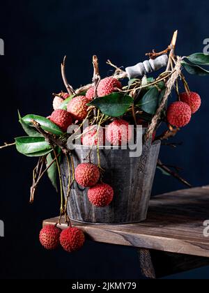 Vorderansicht von frischen reifen Litschi-Früchten mit grünen Blättern in einem Metallkorb auf einem Holztisch Stockfoto