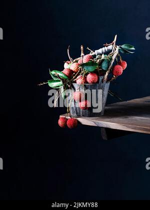 Vorderansicht von frischen reifen Litschi-Früchten mit grünen Blättern in einem Metallkorb auf einem Holztisch Stockfoto