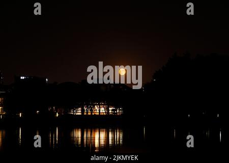 Ein faszinierender Blick auf einen Mond am dunkelschwarzen Himmel über einem Gebäude mit der Spiegelung des Wassers in der Nacht Stockfoto