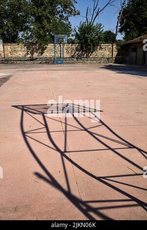 Leerer Basketballplatz, an einem sonnigen Tag von einer Schiene begrenzt Stockfoto