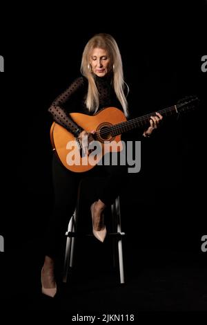 Blonde Frau mit Gitarre im Studio auf schwarzem Hintergrund Stockfoto