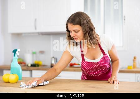 Frau putzt Esstisch mit Lappen in der Küche zu Hause Stockfoto