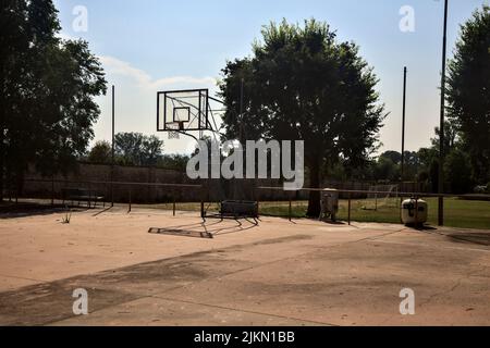 Leerer Basketballplatz, an einem sonnigen Tag von einer Schiene begrenzt Stockfoto