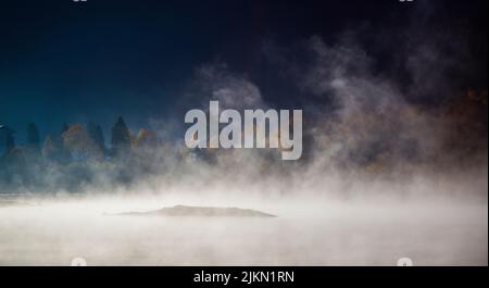 Eine malerische Aussicht auf einen herbstlichen Wald durch den Nebel über dem Wasser Stockfoto