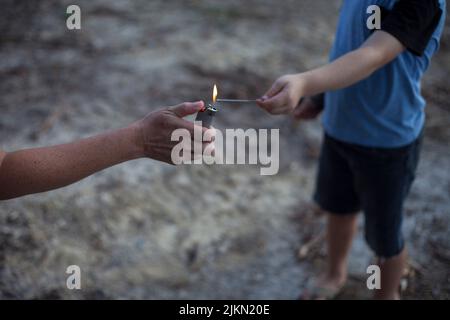 Die Hand der Frau streckt sich mit einem Feuerzeug aus, um den Sparkellerstick eines Kindes anzuzünden. Stockfoto