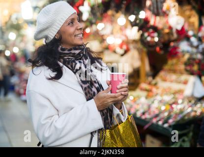Lächelnde hispanische Frau mit einer Tasse warmem Getränk beim Weihnachtsmarkt Stockfoto