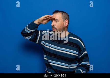 Ein hispanischer Mann in einer gestreiften Bluse, der die Hand auf seine Stirn legt und weit weg schaut Stockfoto