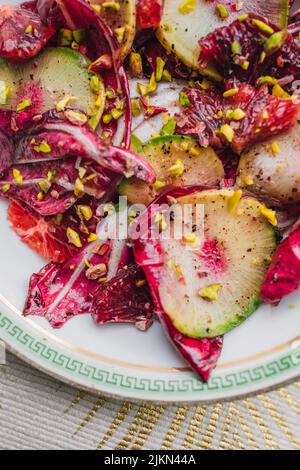 Radicchio Salat mit Wassermelone Rettich, Blutorange, Pistazien auf weißem Teller mit grünem griechischen Schlüssel Stockfoto