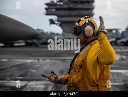 220801-N-DW158-2103 PHILIPPINISCHES MEER (AUG 1, 2022) Aviation Boatswain’s Mate (Handling) 1. Klasse Michael Smith aus Cebu, Philippinen, steuert Flugzeuge auf dem Flugdeck des einzigen vorwärts eingesetzten Flugzeugträgers der US Navy USS Ronald Reagan (CVN 76) in der philippinischen See, 1. August. Ronald Reagan, das Flaggschiff der Carrier Strike Group 5, stellt eine kampfbereite Kraft zur Verfügung, die die Vereinigten Staaten schützt und verteidigt und Allianzen, Partnerschaften und kollektive maritime Interessen in der Indo-Pazifik-Region unterstützt. (USA Navy Foto von Mass Communication Specialist 3. Class Grey Gibson) Stockfoto