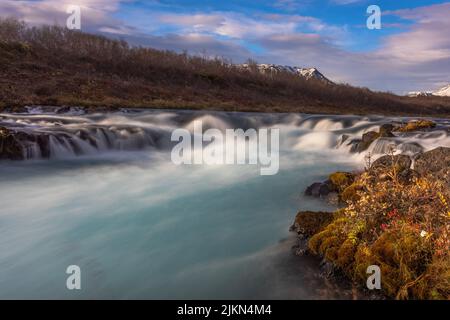 Eine wunderschöne Landschaft des Bruarfoss Wasserfalls auf Felsen vor einem blau bewölkten Himmel in Brekkuskogur, Island Stockfoto